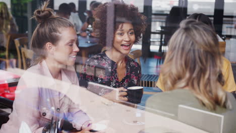 four young female friends meeting sitting at table in coffee shop and talking viewed through window