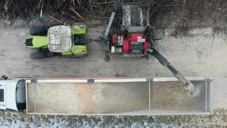 Drone-hover-above-tractor-with-wood-chipper-blow-shredded-wood-in-trailer