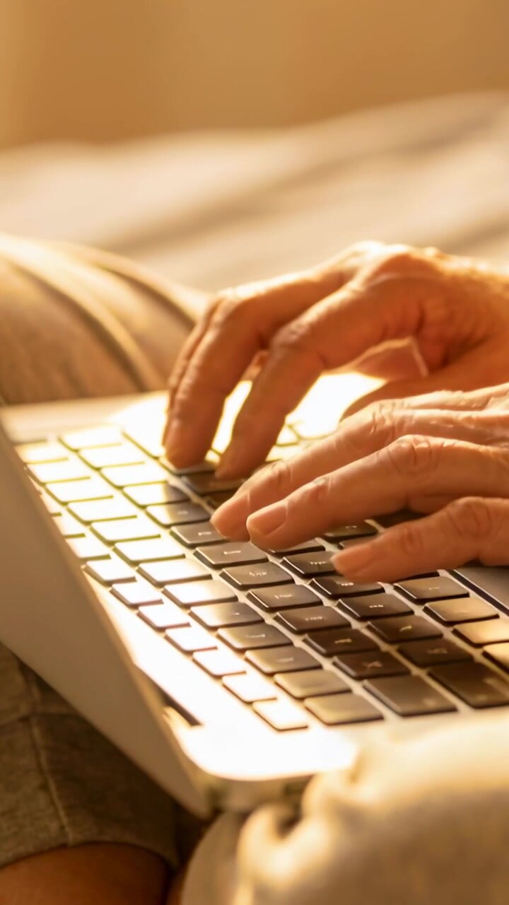 Vertical video: Starting senior hands typing on laptop on lap in bed, working while wearing shorts