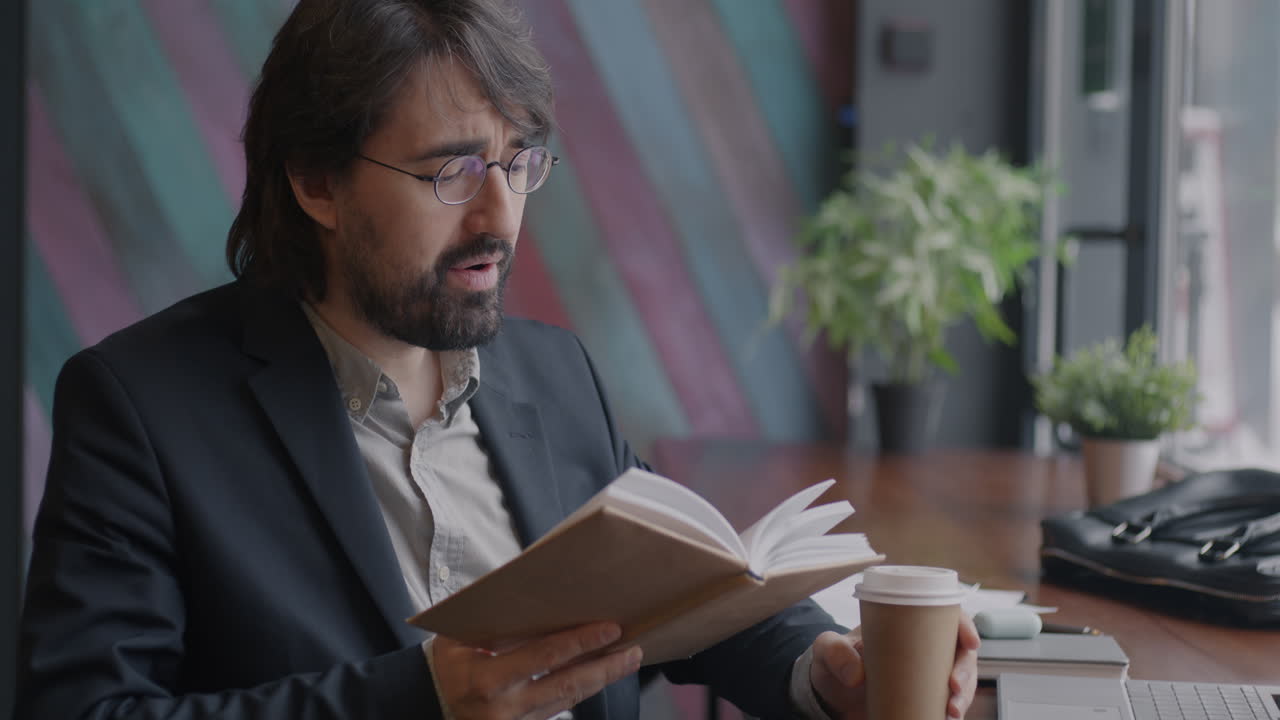 Man Reading a Book and Drinking Coffee in a Cafe