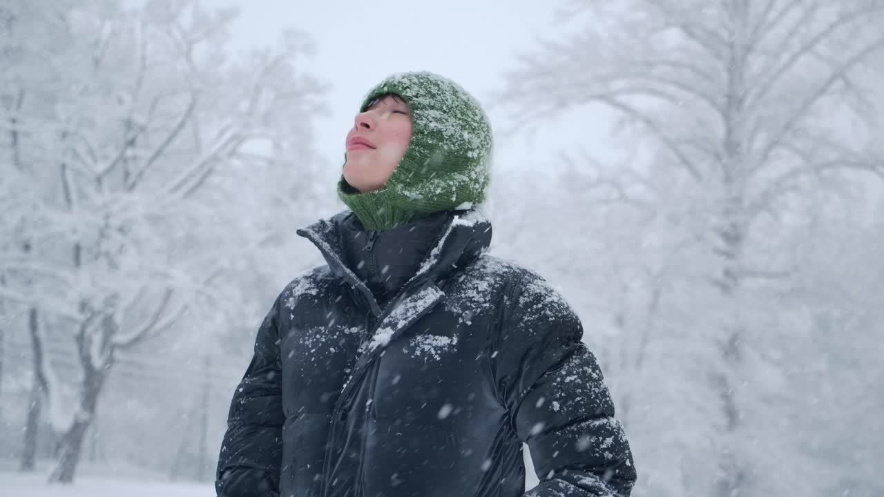 녹색 헤드과 검은색 재을 입은 아름다운 여성이 숲에서 녹는 눈이 나무에서 떨어지면서 느린 동작 영상을 촬영하고 있습니다.