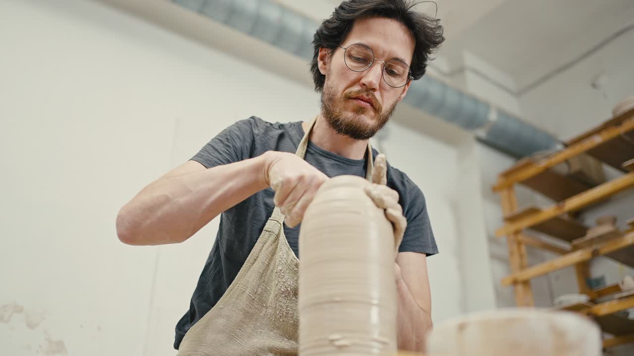artista masculino profesional que crea un jarrón de cerámica, trabajando con arcilla en una rueda de cerámica, vista de abajo, cámara lenta
