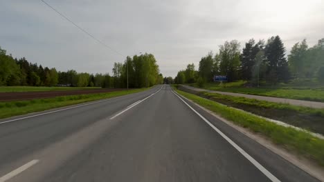 The-road-is-lined-with-green-trees-as-cars-pass-by