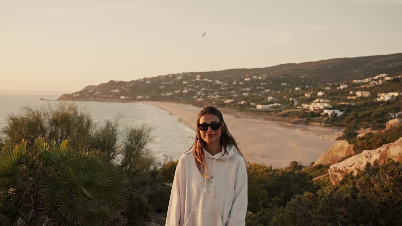 zoom en el disparo de la cámara de la mujer con gafas de sol posa para la cámara con la playa en el fondo
