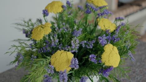 ramo de flores amarillas y púrpuras con follaje verde, arregladas hermosamente, destacando la elegancia natural
