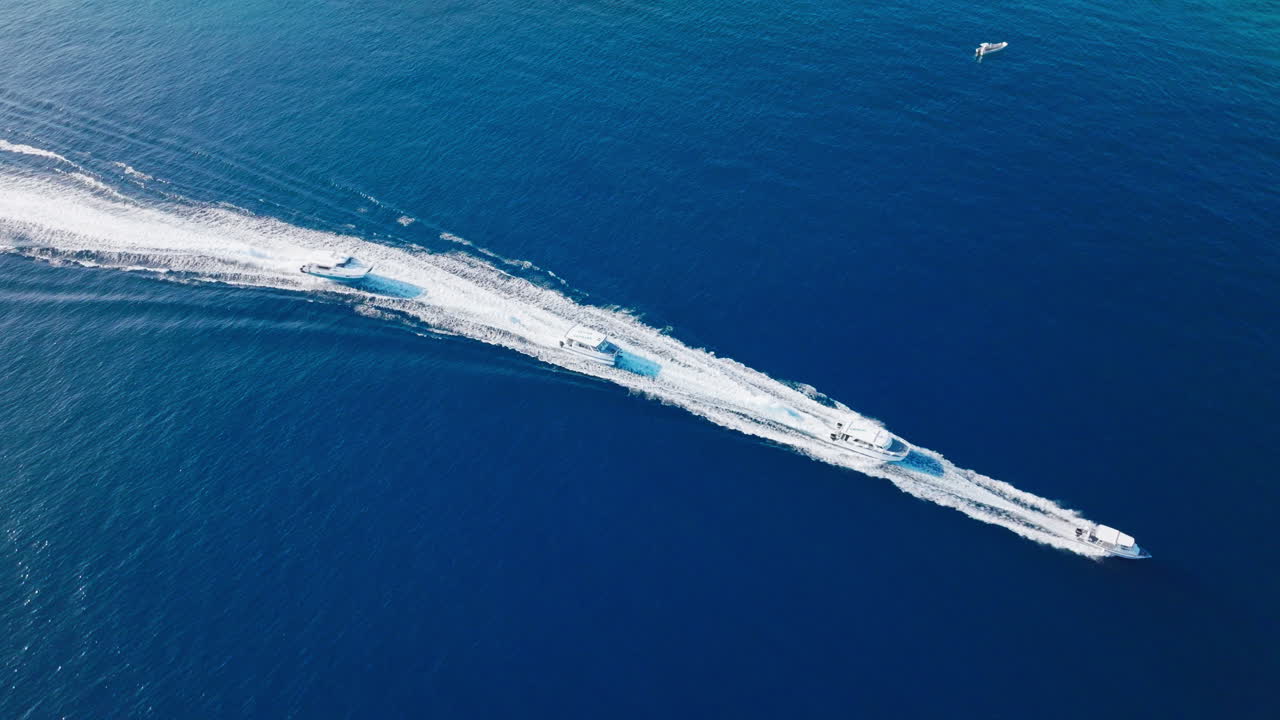 Aerial drone of white boat cruising over deep blue ocean leaving long trail of wake