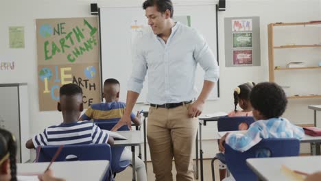 happy diverse male teacher and children writing at desks in elementary school class, slow motion