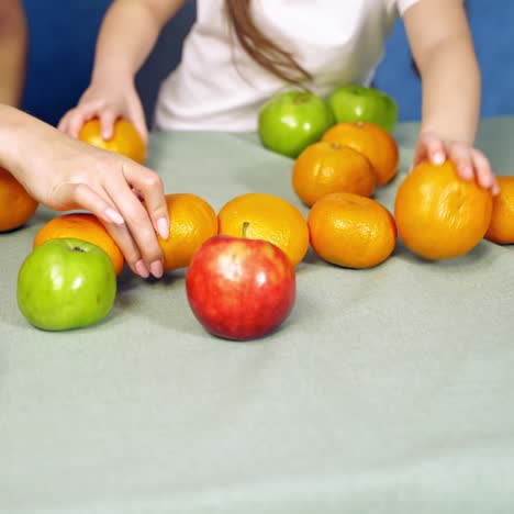 fresh organic fruits on the table. woman and a little girl playing with tangerines and apples on white background. close-up.