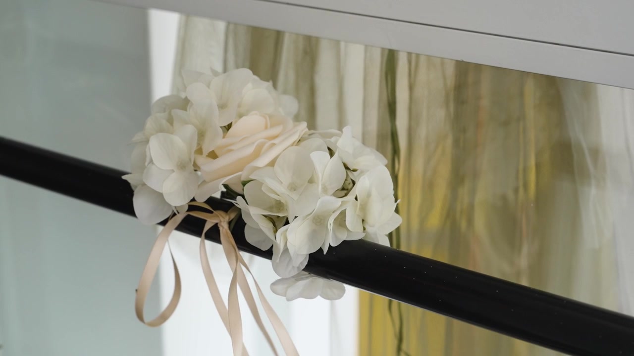 A close view of a floral arrangement on a railing with white flowers and a ribbon. The setting has natural light and a mirror reflects the environment around it.