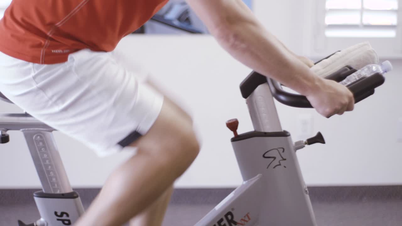 Man is engaged in a bicycle simulator in the gym. The guy is exercising on a stationary bike.