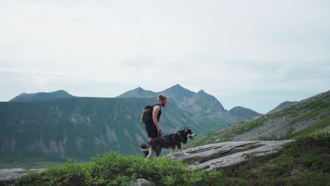 hiker with backpack holding the leash of siberian husky while walking up on salberget hill norway