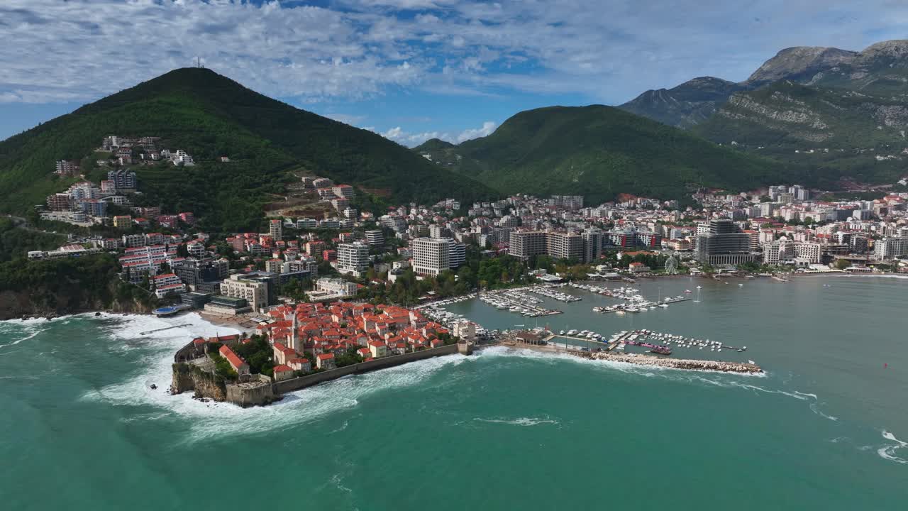 Aerial pan shot of Budva town with green hills at background in Montenegro during daytime.
