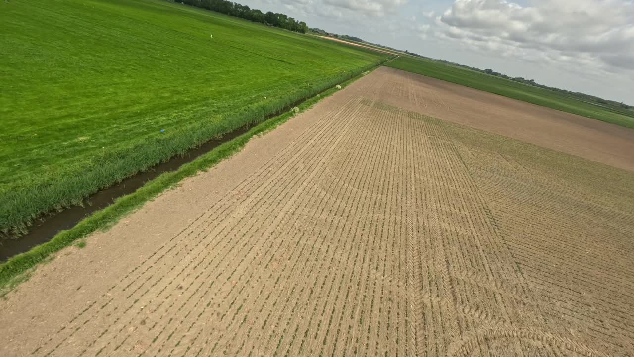 Drone flying over a waterway in between farm fields during a summer day
