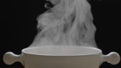 the hot tea in the white cup has white smoke and steam effect on the black background.