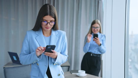 smartphones in the hands of female young employees in office. long-haired ladies in glasses holding handsets and scrolling screens. blurred backdrop.