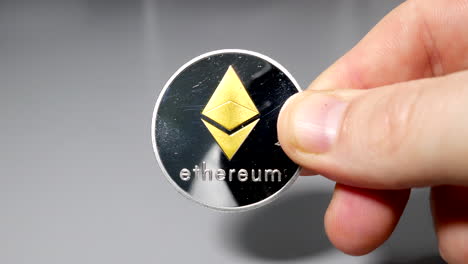 silver and ethereum bitcoin coin held between fingers in hand on gey table