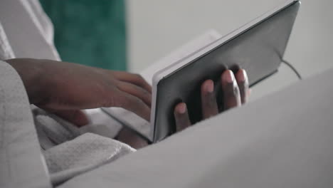 close-up of man in white bathrobe holding black notebook, turning pages, soft light illuminating hands, green velvet headboard in background, relaxed indoor setting