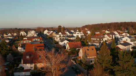 Forward-flying-drone-over-streets-with-family-houses-in-neighbourhood.-Aerial-view-of-small-town-in-evening-golden-hour.-Bad-Vilbel,-Germany.