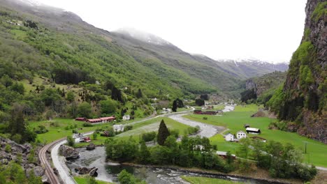 Aerial:-Flåm-train-descending-a-mountain-side-among-green-meadows-in-a-valley