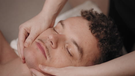 adult man is relaxing in spa salon masseuse is massaging his face for relax and recreation closeup view
