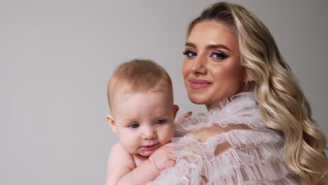 caucasian woman with blonde wavy hair holding a baby. happy young mother with her son in hands. white backdrop.