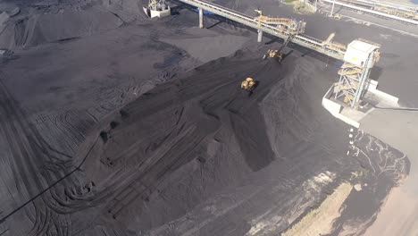 aerial drone shot of coal mine plant, coal coming off conveyor belt with caterpillar mining trucks moving the coal around