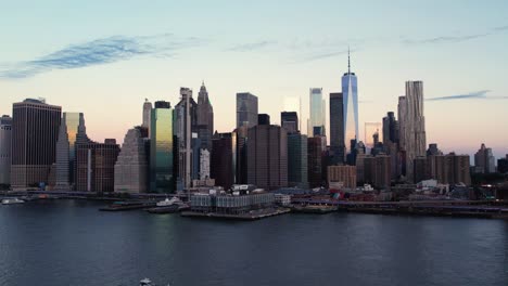 Aerial-view-of-a-ferry-in-front-of-the-Manhattan-cityscape,-dawn-in-NYC,-USA---ascending,-drone-shot