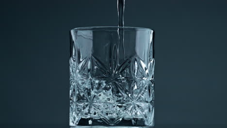 water pouring crystal glass at dark background closeup. fresh liquid filling