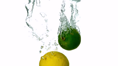 limón y limón sumergiéndose en el agua sobre un fondo blanco