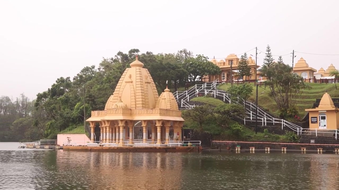 Panoramaudsigt over den hellige hinduistiske tempelarkitektur ved Ganga Talao, Grand Bassin, Mauritius, beliggende ved bredden af en hellig vulkansk kratersø omgivet af frodig bjergvegetation.