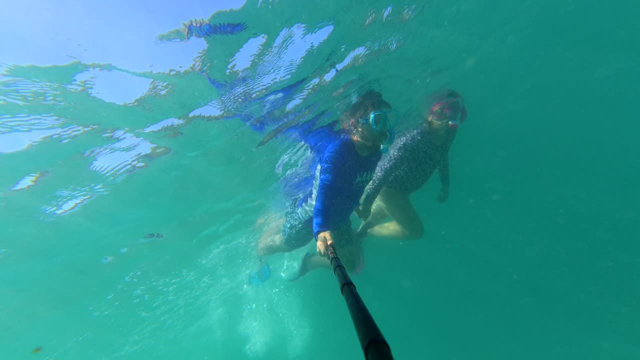 Pareja buceando. Una persona sujeta un palo selfie para capturar el momento bajo el agua en Tenacatica, Jalisco, México. - Toma submarina
