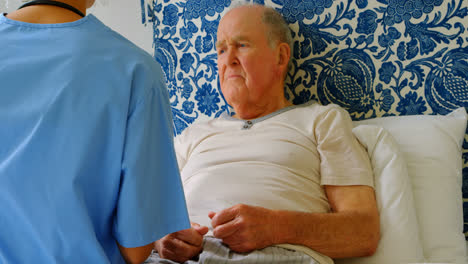 Rear-view-of-young-Caucasian-female-doctor-discussing-medication-with-senior-man-on-bed-at-home-4k