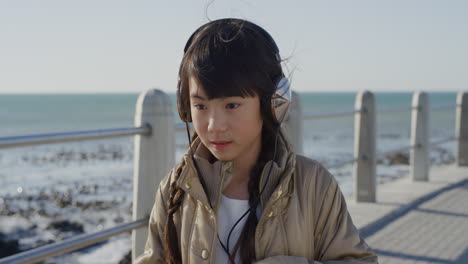 portrait-beautiful-little-asian-girl-looking-serious-calm-little-kid-wearing-headphones-listening-to-music-on-sunny-seaside-beach-slow-motion