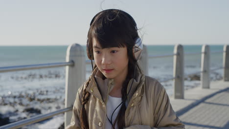 retrato de una hermosa niña asiática que parece seria, tranquila, un niño con auriculares escuchando música en una playa soleada a cámara lenta