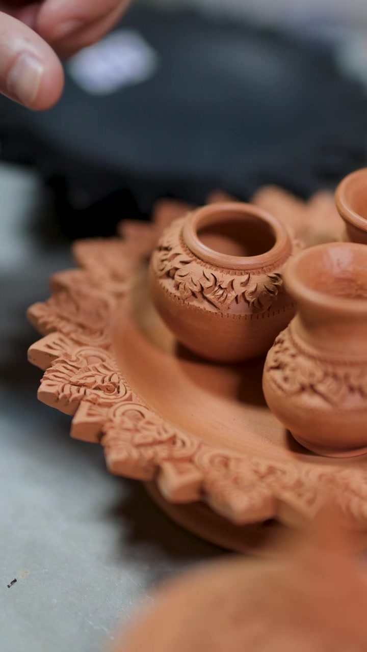 Primo piano delle mani che sistemano intricate miniature di vasi in ceramica su un tradizionale vassoio di argilla intagliato.