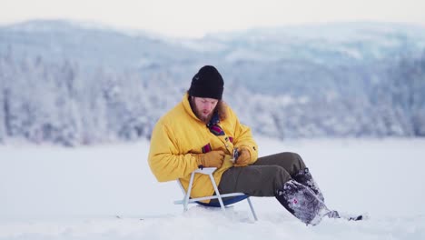 Mann-Sitzt-Auf-Einem-Zugefrorenen-See-Zum-Angeln---Eisfischen-In-Indre-Fosen,-Norwegen---Breit