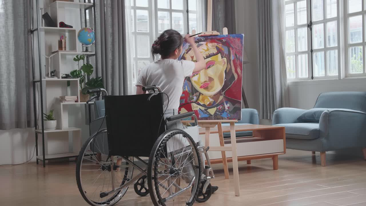 vista posterior de una artista talentosa sentada en una silla de ruedas, usando con entusiasmo el pincel que crea con pintura al óleo. estudio creativo con lienzo