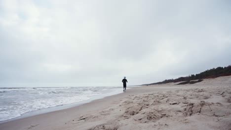 runner with black sportswear is running in the beach away from camera