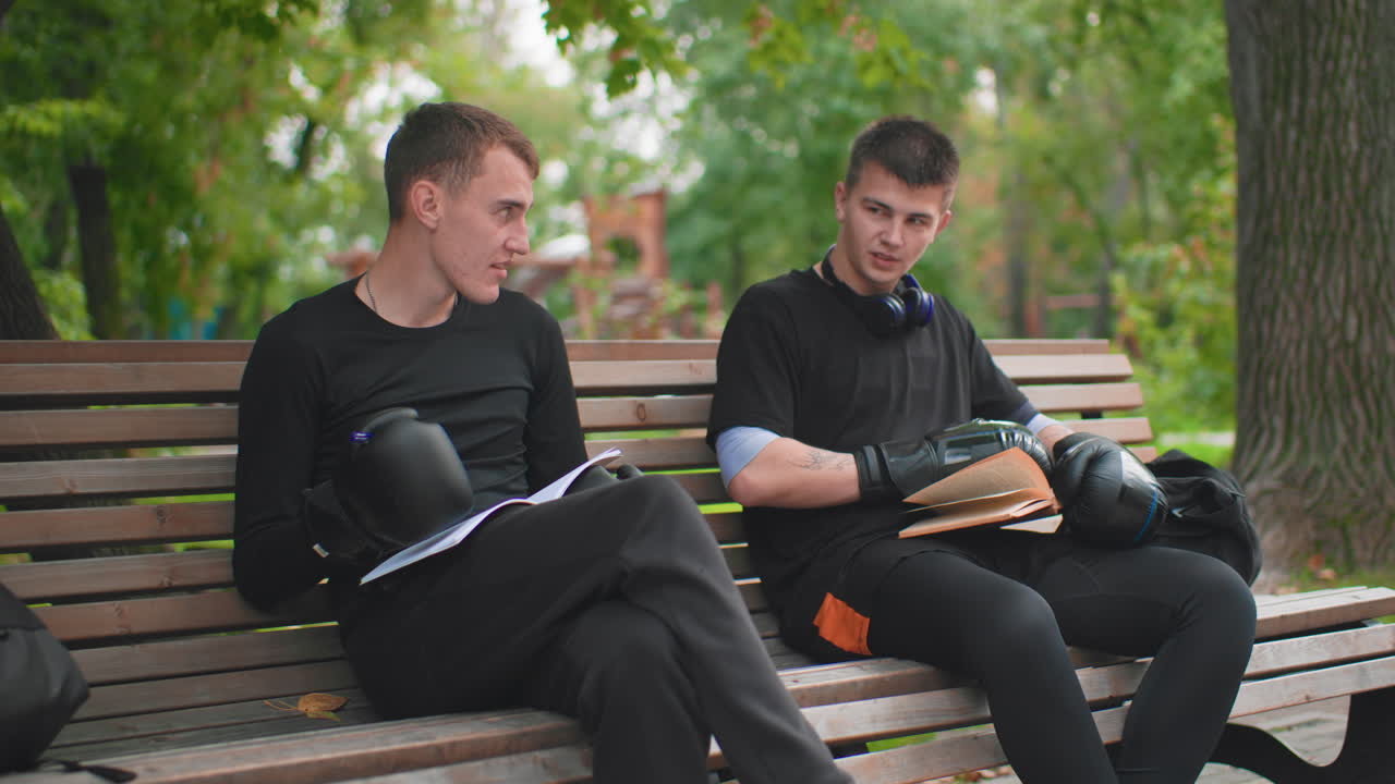 Dois homens examinando cuidadosamente equipamentos de equitação, cena de parque urbano com homens inspecionando equipamentos de proteção para motocicleta, dois indivíduos revisando minuciosamente capacete e luvas em um parque da cidade antes de andar de bicicleta