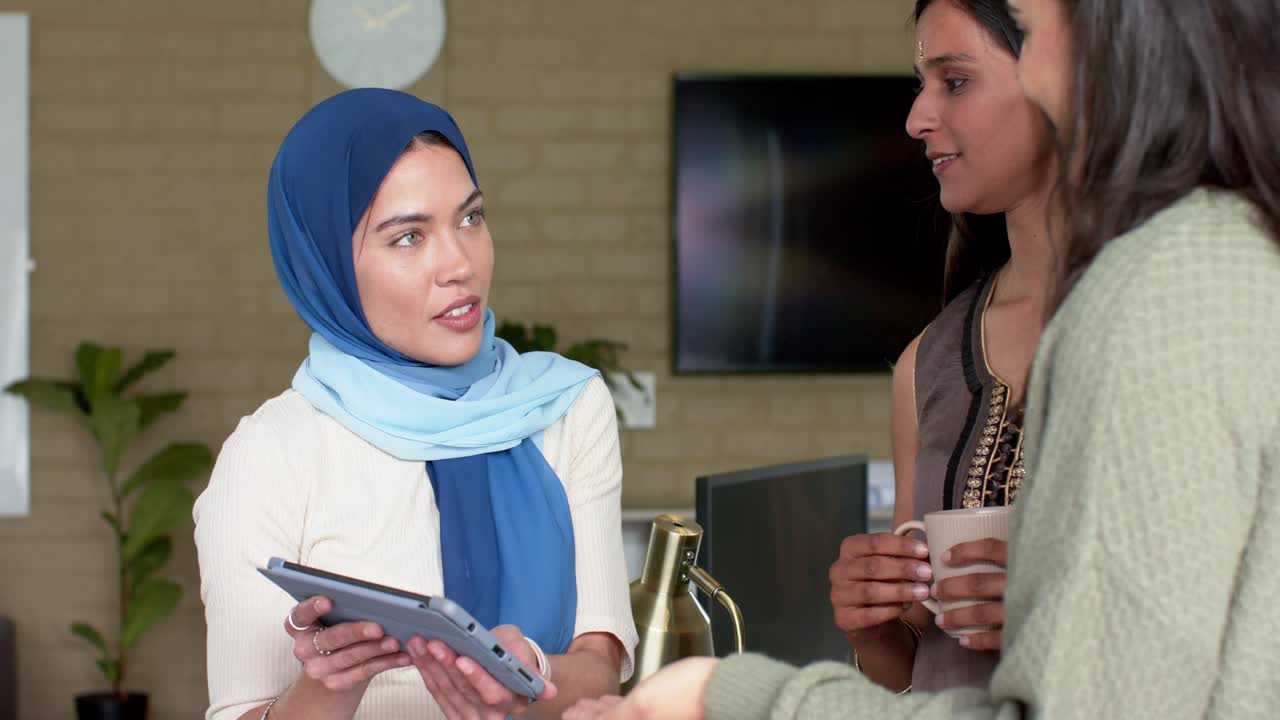 Wanita berhijab mengenakan sweter hijau memberi isyarat ke arah tablet, mengetuk, menggesek demo, dan tim mengawasi di konter