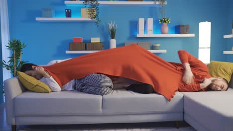 two brothers cannot share the blanket while they are lying on the sofa at home.