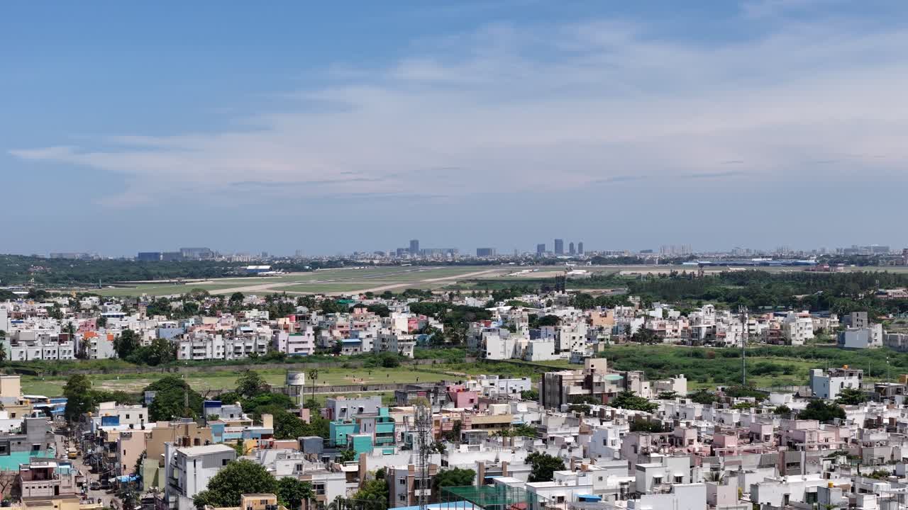 A wide, daytime shot overlooking a dense residential area with an airport runway in the mid-ground and a modern city skyline on the horizon. flight landing in the long distance