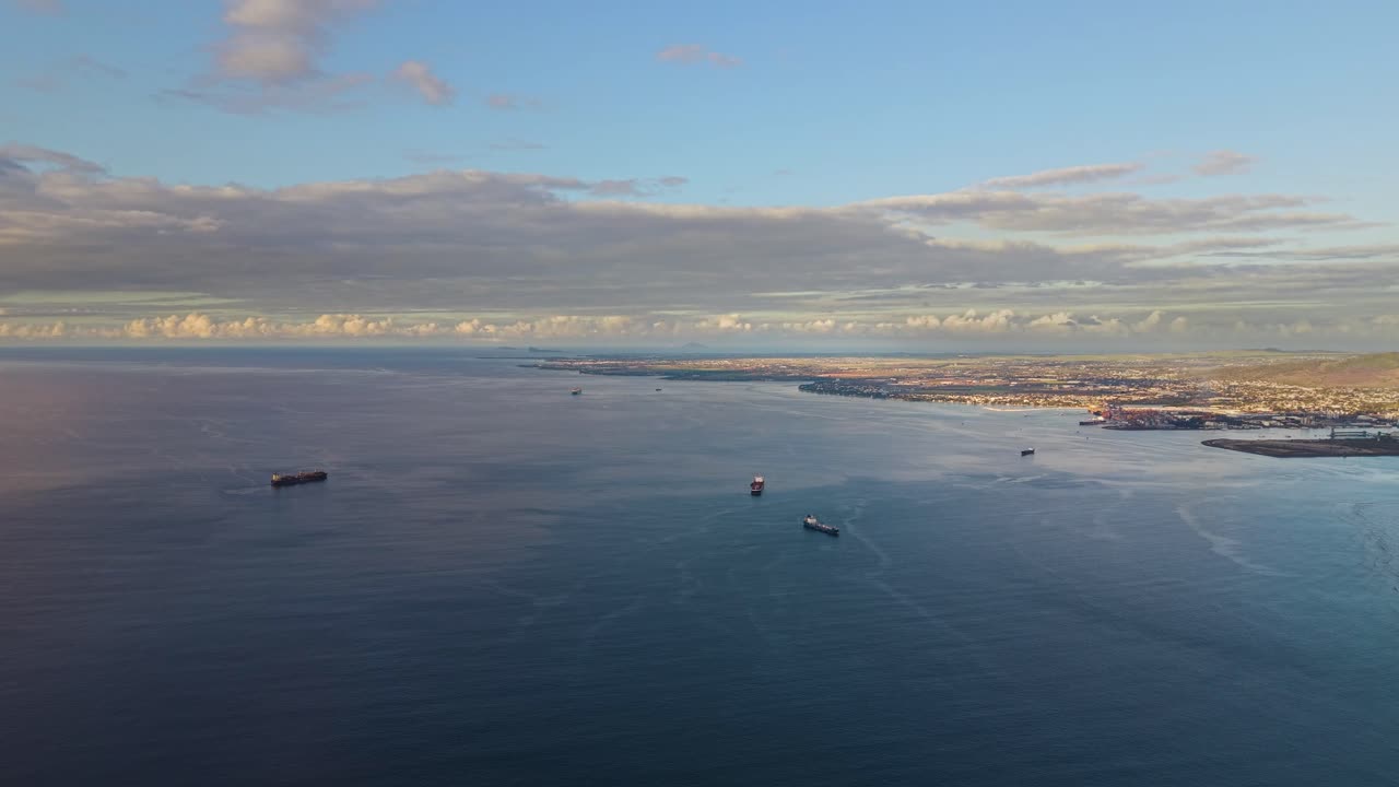 Wide aerial shot of Oil tankers anchored off the Mauritius coastline at sunset, reflecting warm light across the tranquil ocean