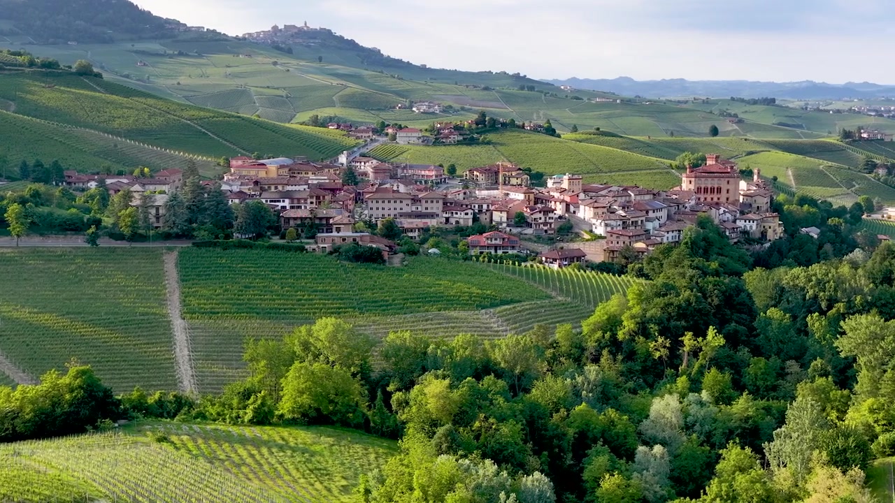 Panorámica aérea amplia de exuberantes colinas ondulantes, arquitectura de pueblos históricos y extensos viñedos italianos