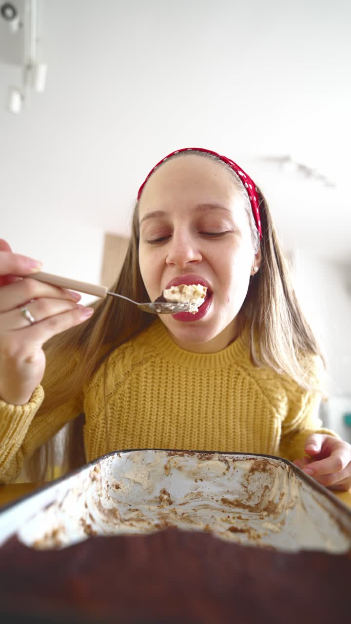 Woman eating tiramisu dessert at home with a joyful expression, enjoying a sweet Italian treat during a relaxed moment of home dining and dessert indulgence