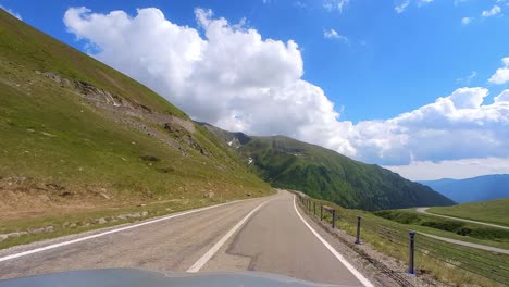 car point of view, the majestic transfagarasan mountain road with a grey car bonnet in the foreground and tall mountain peaks and a clear blue sky in the background