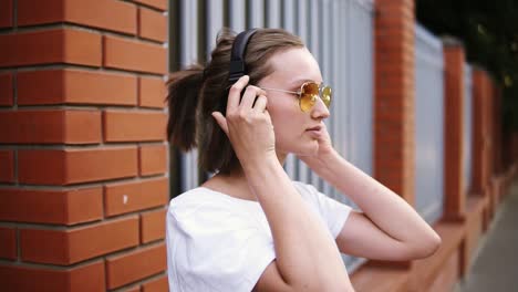 una chica con un corte de pelo corto, con gafas de sol amarillas. relajada apoyada en la valla, escuchando su música favorita en negro