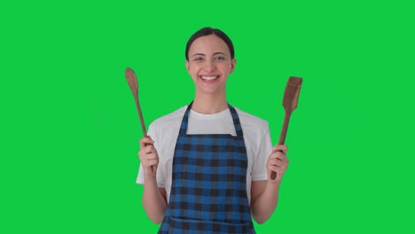 ama de casa india feliz posando con cuchara y espátula pantalla verde