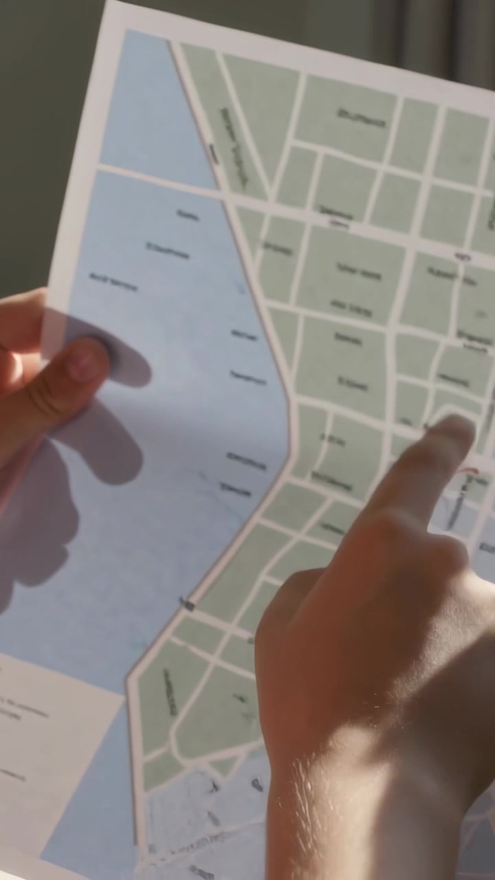 Video vertical: Niño ajustando papel y trazando una ruta roja en un mapa en una mesa cerca de una ventana, con espacio para texto.