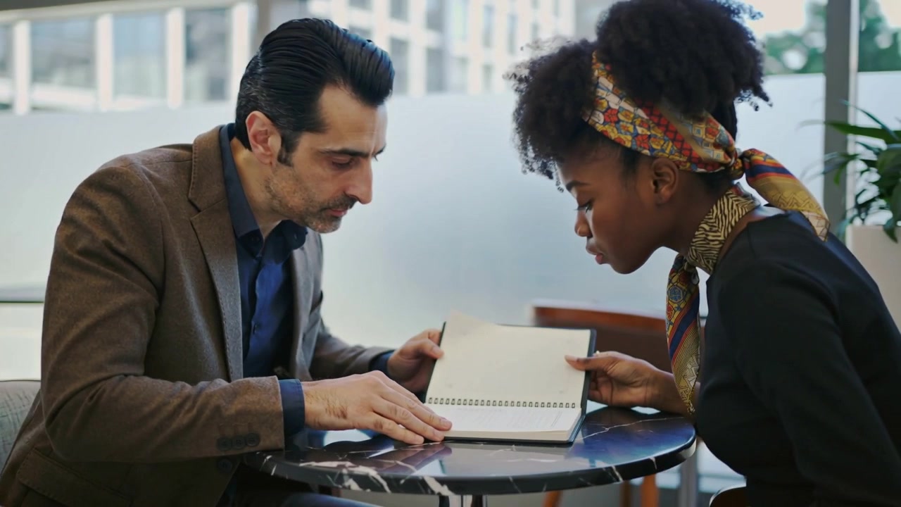 Placing spiral notebook, man in brown suit and woman in scarf opening page during office meeting
